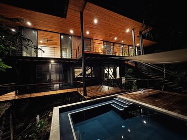 Modern two-story house with wooden accents and a lit pool at night.