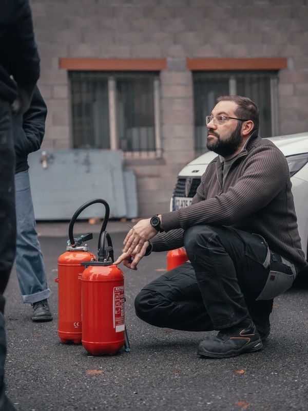 Homme accroupi près d'extincteurs rouges.