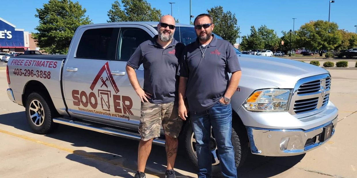 Two men standing by a silver truck with construction business branding.