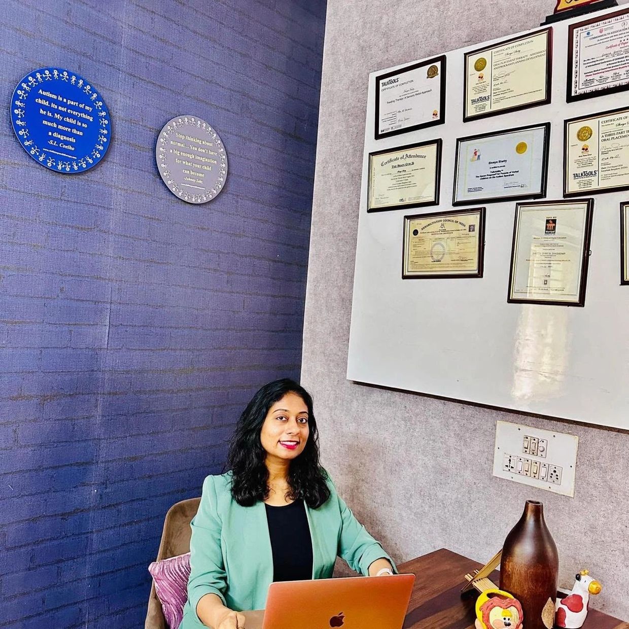 Woman working on laptop in office with certificates on wall.