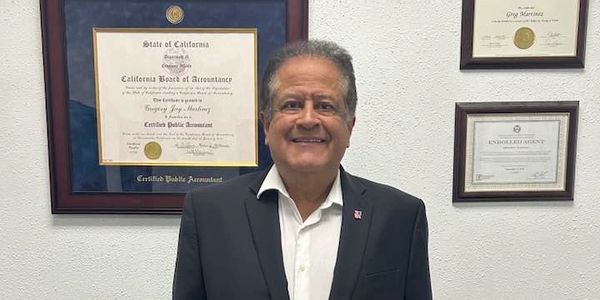 Man in suit standing in front of framed certificates on a wall.