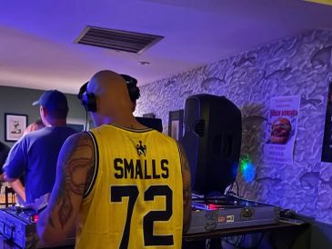 DJ Smalls wearing a yellow jersey with headphones in a club setting.