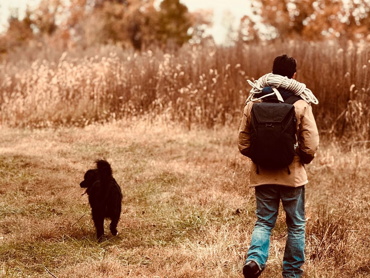Man hiking with a dog in an autumn field.