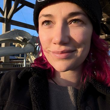 Woman with purple hair and black beanie smiling outdoors.