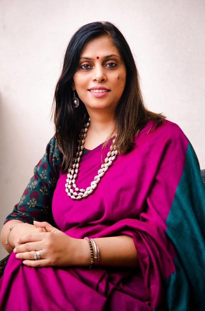 Woman in a magenta saree with a pearl necklace smiles gently at the camera.