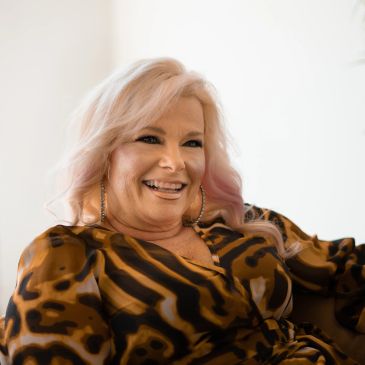 Smiling woman with pinkish blonde hair in a patterned top.