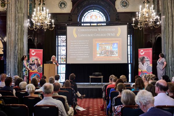 Audience at a formal presentation in an ornate hall.