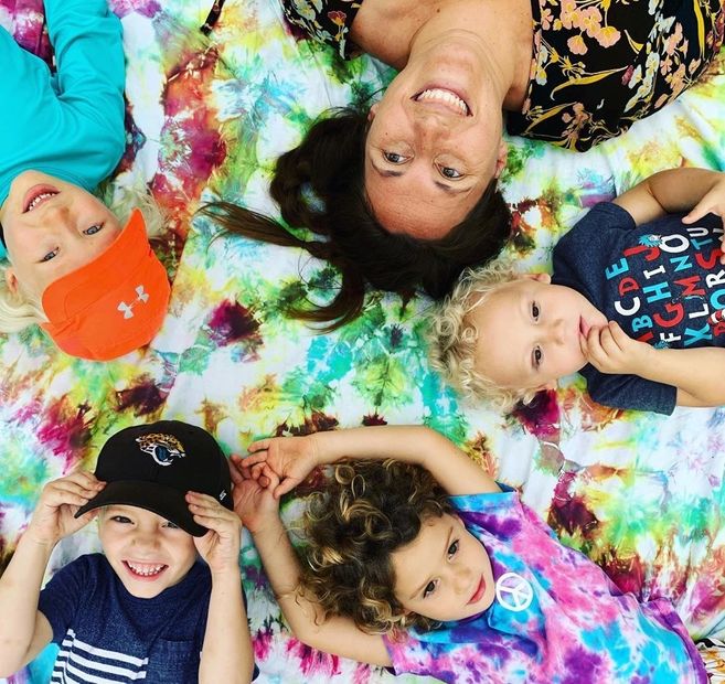 Group of children with teacher laying on tie dye blanket. 