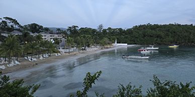 Calm beach with boats anchored near the shore and palm trees lining the coast.
