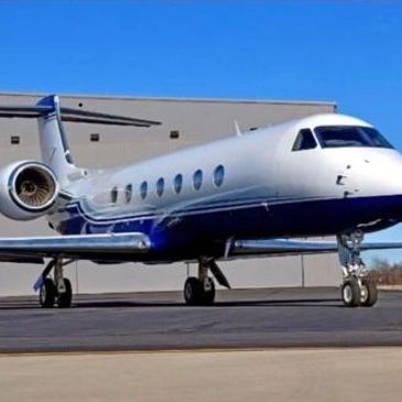 A sleek private jet parked on the tarmac under a clear blue sky.