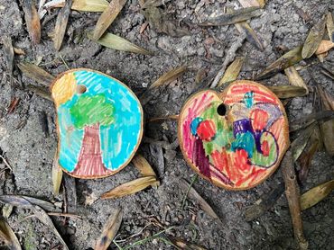 Two wooden discs painted with colorful designs on dirt and leaves.