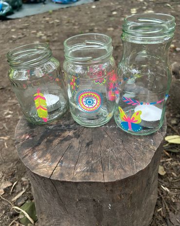 Three decorated glass jars with candles on a tree stump outdoors.