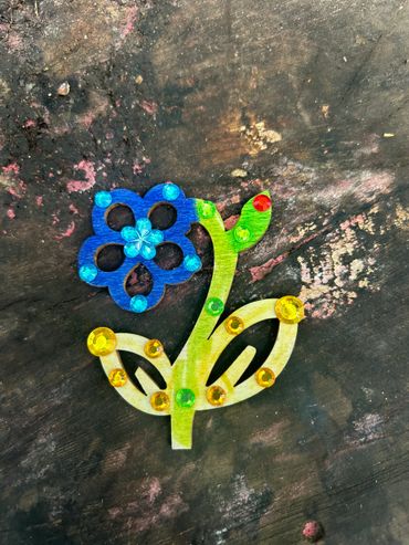 Colorful wooden flower decorated with shiny beads on a worn surface.