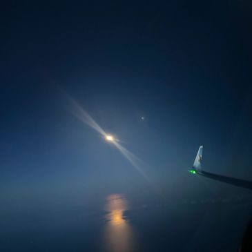 View of moon over water from an airplane window at night.