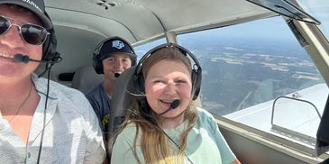 Three people smiling inside a small airplane cockpit.