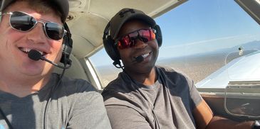 Two men smiling inside a small airplane cockpit.