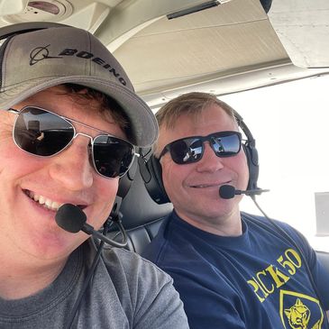 Two men wearing headsets and sunglasses inside an aircraft.