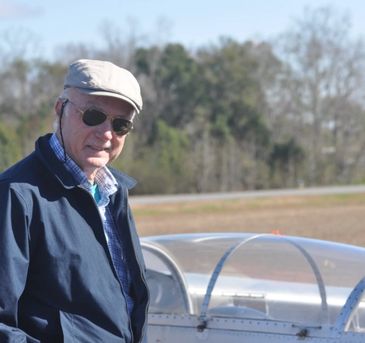 Older man standing near a small airplane outdoors.