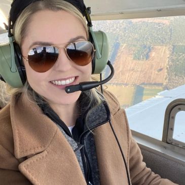 Woman smiling inside a small aircraft wearing headphones and sunglasses.