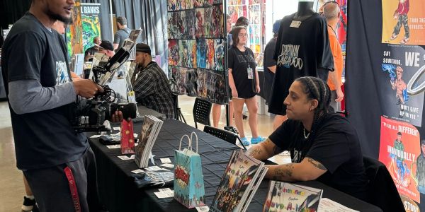Comic convention artist table with people interacting.