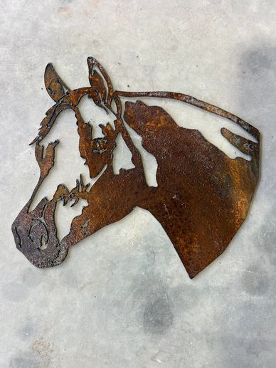 Rusty metal art of a horse's head on a concrete floor.