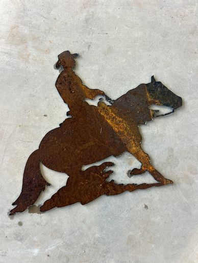 Rusty metal silhouette of a cowboy riding a horse against a concrete background.