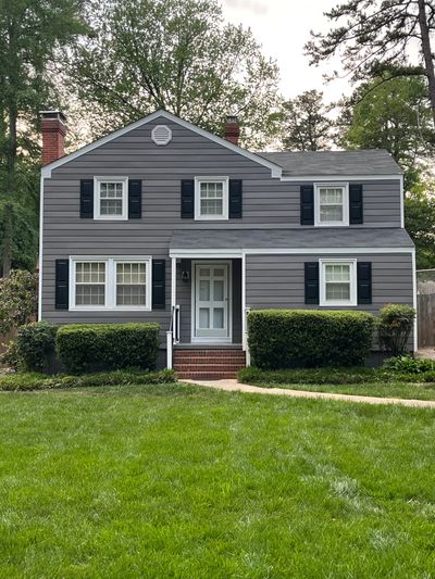 Gray two-story house with black shutters and green lawn.