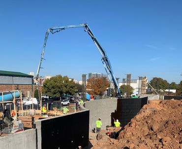 Construction workers use a concrete pump to build a curved concrete wall on a sunny day.