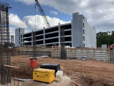 Large concrete parking structure under construction with crane and rebar columns.
