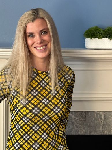 Therapist Jamie Papadakis in a yellow and black plaid shirt in front of a fireplace