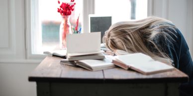 woman exhausted at desk and head on a pile of books