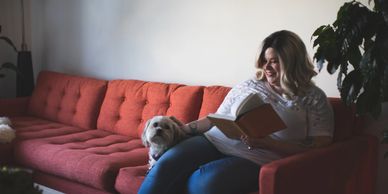 woman reading a book sitting on couch with her dog