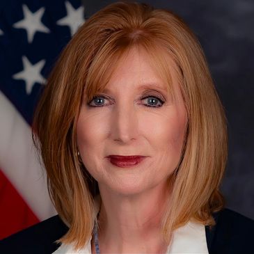 Professional portrait of a middle-aged woman with red hair and an American flag background.