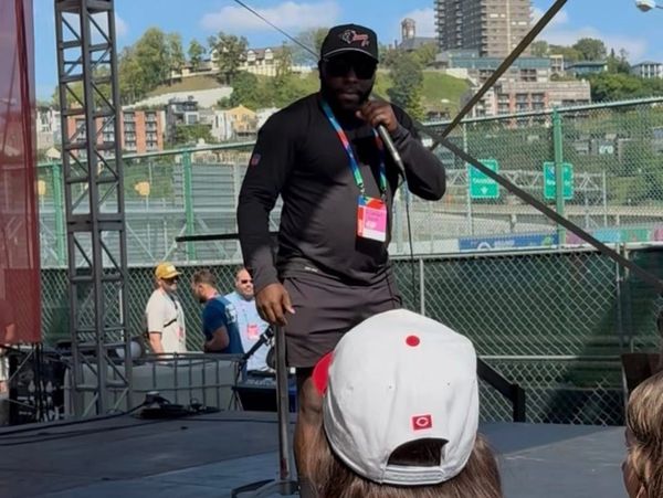 Man in black performing on stage with microphone outdoors during the day.