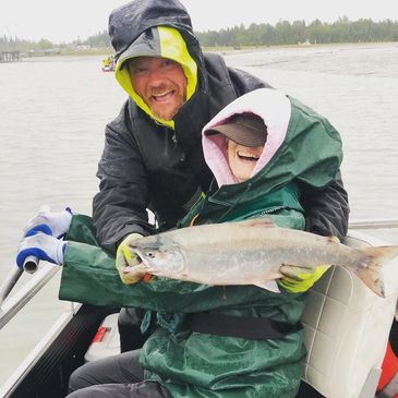 Two people in rain gear holding a large fish on a boat.