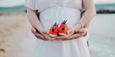 Hands holding baby shoes over a pregnant belly.
