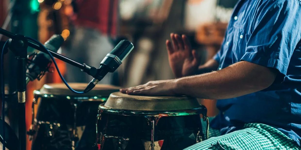 A musician playing conga drums with microphones set up for recording.