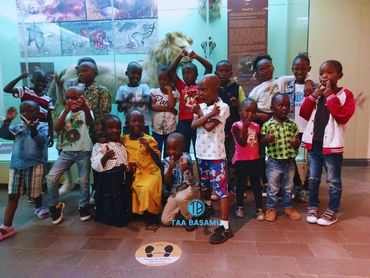 Group of children posing playfully in a museum with a lion exhibit behind them.