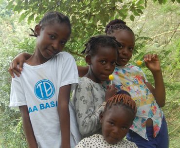 Four girls enjoying lollipops outdoors surrounded by trees and greenery.
