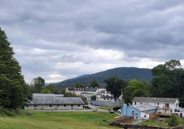 A green field with buildings and hills under a cloudy sky.