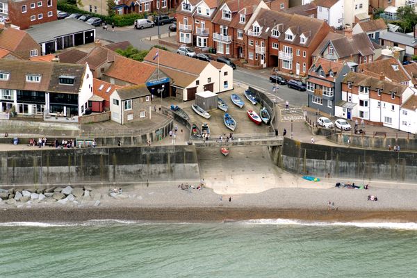 Seaside village with boats and people near a pebble beach and promenade.