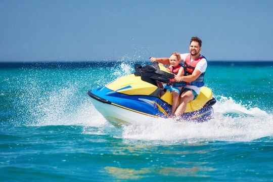 Father and child riding a jet ski on the ocean.