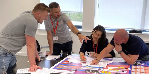 Four colleagues collaborate over documents and charts at a table in a bright office.