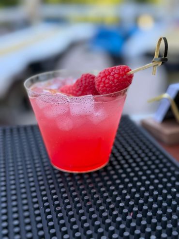 A refreshing pink cocktail with ice and fresh raspberries garnish.