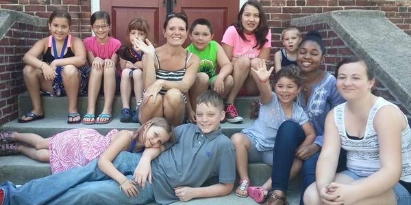 A diverse group of children and adults smiling on outdoor steps.