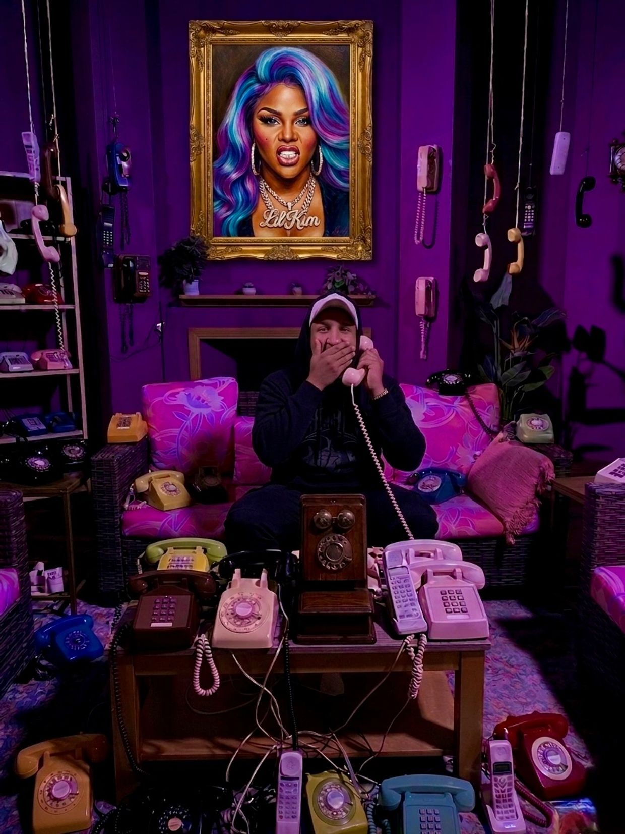 Man in a purple room surrounded by vintage telephones, sitting under a colorful Lil Kim portrait.