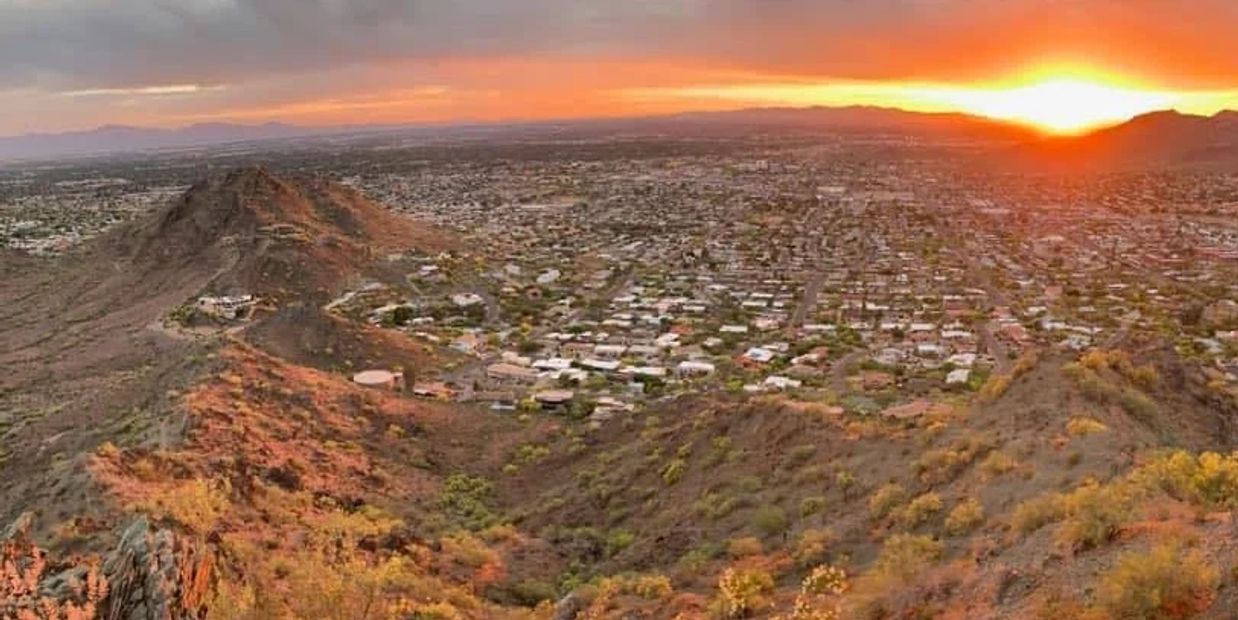 Sunset over a sprawling cityscape with rocky hills in the foreground.