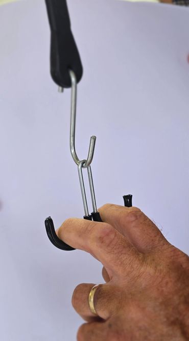 Hand gripping a black-handled metal tool with three prongs.