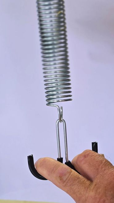 Close-up of a hand gripping a metal spring with hooks.