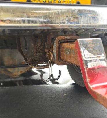 Rusty trailer hitch with fishing hooks hanging underneath a truck.